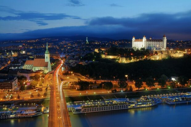 A night view of Bratislava shows illuminated castle and city roads beside the river, 2K Desktop Wallpaper