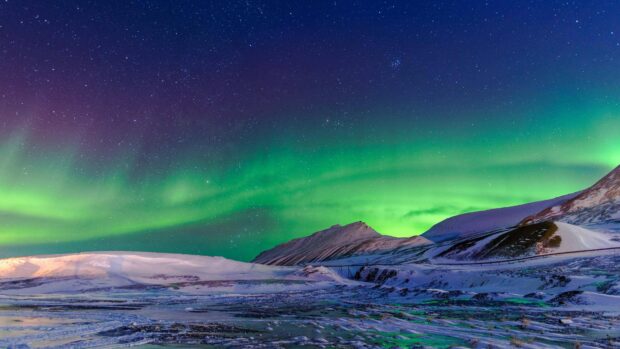 The Arctic displays vibrant northern lights above snow covered mountains at night, 4K Desktop Wallpaper