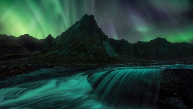 The Arctic landscape shows northern lights dancing above a rugged mountain and flowing river, 4K Desktop Wallpaper
