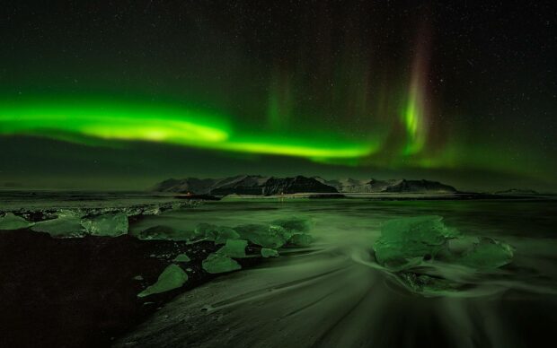 The Arctic wallpapers display a vibrant green northern lights show above icy shores and dark mountains, HD Desktop Wallpaper
