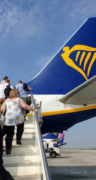 Passengers are climbing stairs to board the Ryanair plane on the tarmac under clear skies, 2K Mobile Wallpaper