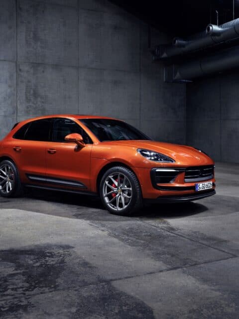 Porsche Macan in vibrant orange parked in modern industrial garage perfect wallpaper background