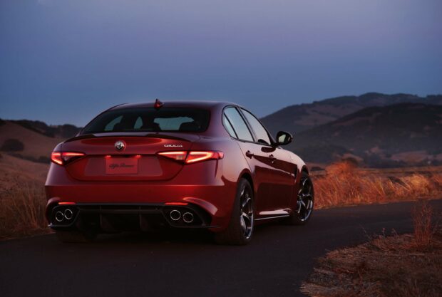 A red Alfa Romeo Giulia is parked on a paved road with hills in the background during dusk, 2K Desktop Wallpaper