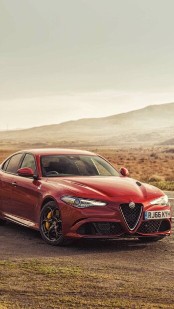A red Alfa Romeo is parked on a rural road with hills in the background showcasing sporty and sleek design, 2K Mobile Wallpaper
