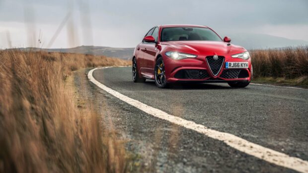 A red Alfa Romeo car is driving on a winding country road surrounded by dry grass, 4K Desktop Wallpaper