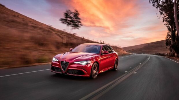 A red Alfa Romeo car is driving fast on a winding road during sunset showing its sleek design, 2K Desktop Wallpaper
