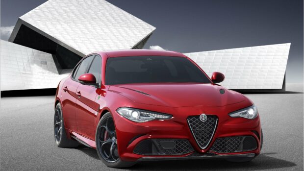 A red Alfa Romeo car is parked in front of a futuristic architectural building, showcasing its sleek design and headlight details