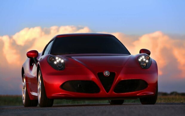 A red Alfa Romeo sports car is parked on a road with a colorful sunset sky in the background, HD Desktop Wallpaper