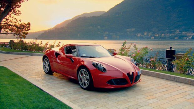A red Alfa Romeo sports car is parked near a lake with mountains and a sunset in the background, HD Desktop Wallpaper