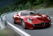 A red Alfa Romeo sports car driving along a winding mountain road surrounded by trees, 2K Desktop Wallpaper