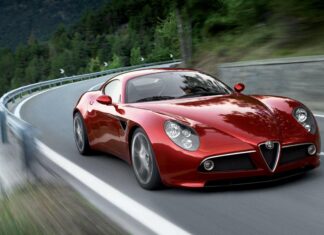 A red Alfa Romeo sports car driving along a winding mountain road surrounded by trees, 2K Desktop Wallpaper
