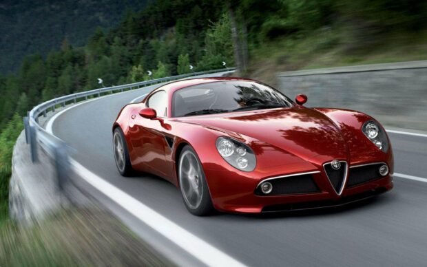 A red Alfa Romeo sports car driving along a winding mountain road surrounded by trees, 2K Desktop Wallpaper