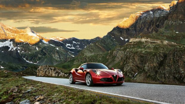 A red Alfa Romeo is parked on a winding mountain road with rocky peaks in the background, HD Desktop Wallpaper
