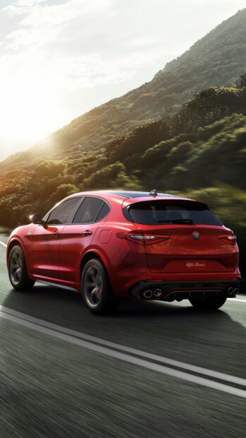 A red Alfa Romeo car is driving along a road with green hills in the background under a bright sky, 4K Phone Wallpaper