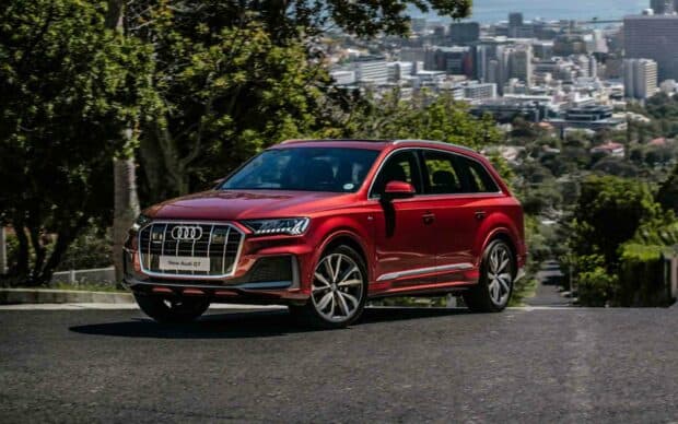 A red Audi Q7 SUV is parked on an asphalt road with a cityscape and greenery in the background, HD Desktop Wallpaper