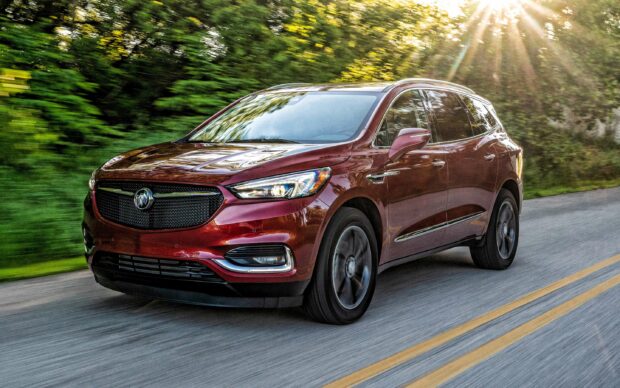 A red Buick Enclave is driving on a forested road with sunlight shining through the trees, 2K Desktop Wallpaper