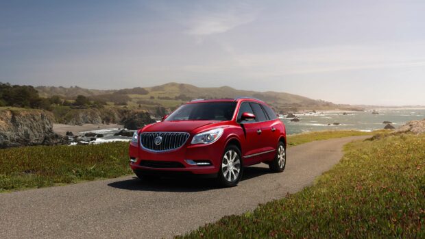 A red Buick Enclave is parked on a coastal road with hills and ocean in the background, 4K Desktop Wallpaper