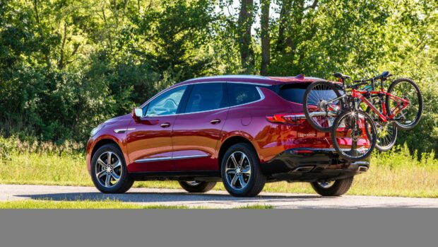 A red Buick Enclave is parked on a road with two bicycles mounted on its rear bike rack surrounded by greenery, 4K Desktop Wallpaper