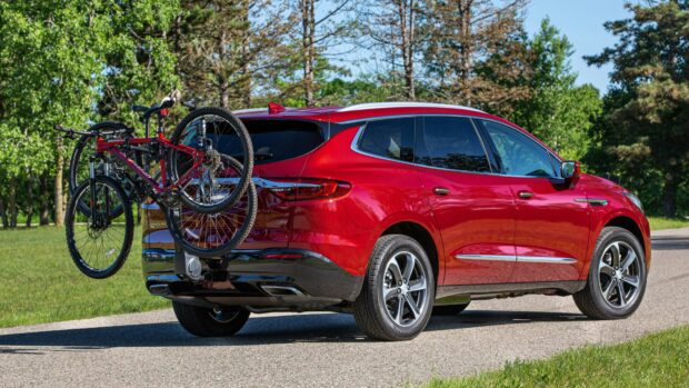A red Buick Enclave is parked on a road with a bike rack attached carrying two bicycles, surrounded by green trees, 4K Desktop Wallpaper