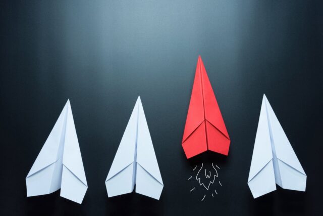 Red Paper Airplane Leading Among White Planes