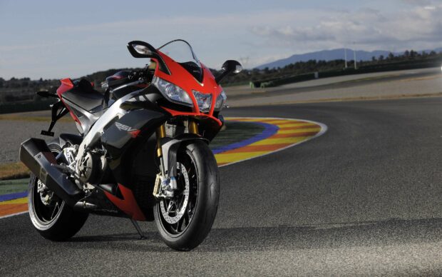 An Aprilia motorcycle is parked on the race track with colorful curbs and mountains in the background, 2K Desktop Wallpaper