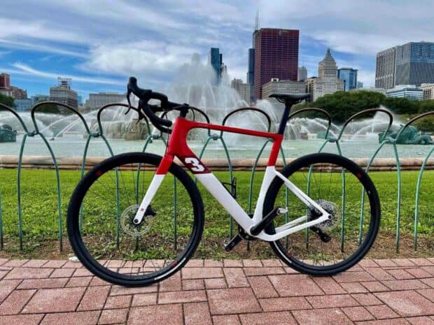 A red and white 3T bike is parked in front of a city park fountain with skyscrapers in the background, HD Desktop Wallpaper