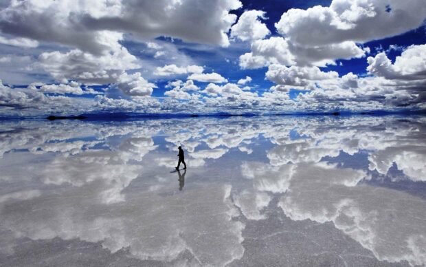 A person walking on the reflective salt flat under dramatic clouds in Bolivia, 2K Desktop Wallpaper