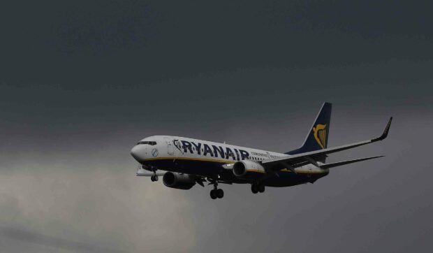 A Ryanair airplane is captured flying through a dark cloudy sky, HD Desktop Wallpaper