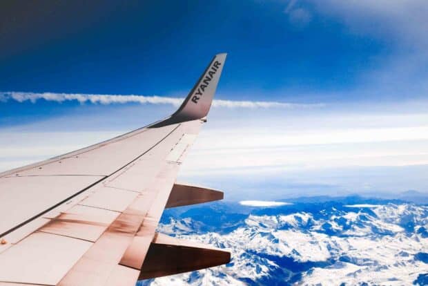 A Ryanair airplane wing flies over snow covered mountains under a blue sky with clouds, HD Desktop Wallpaper