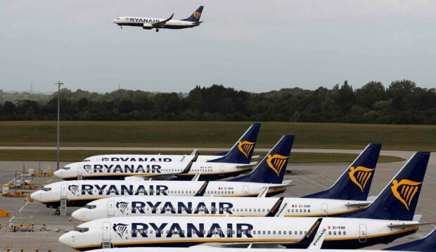 A lineup of Ryanair airplanes is parked at the airport with one Ryanair plane flying overhead, 2K Desktop Wallpaper