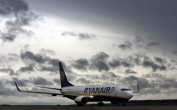 A Ryanair plane is taxiing on a runway with a cloudy sky overhead, 2K Desktop Wallpaper