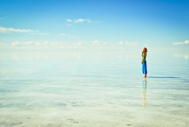 A woman stands on the reflective salt flats under a bright blue sky in Bolivia showcasing tranquility, 2K Desktop Wallpaper