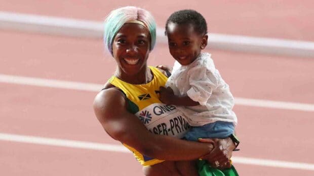 Shelly Ann Fraser Pryce is smiling while holding a young child on a running track, HD Desktop Wallpaper