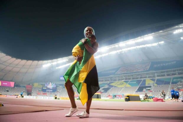 Shelly Ann Fraser Pryce holding a child wrapped in the Jamaican flag on the stadium track after a race, 2K Desktop Wallpaper