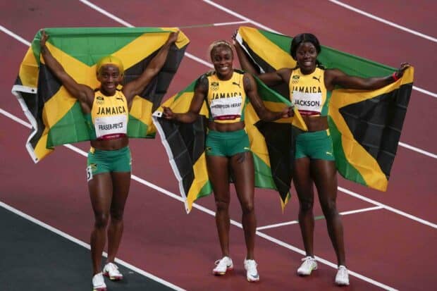 Shelly Ann Fraser Pryce is standing proudly with her Jamaican teammates holding their flags after a race, 2K Desktop Wallpaper