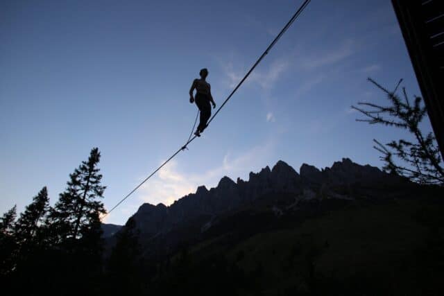 Silhouette of person slacklining high above forest with mountain background at dusk