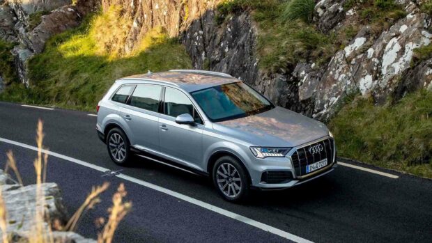 A silver Audi Q7 drives along a winding mountain road surrounded by rocky cliffs and grassy hills, HD Desktop Wallpaper