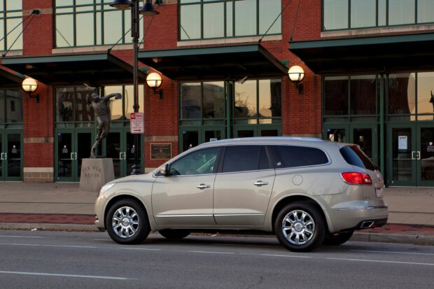 A silver Buick Enclave is parked beside a brick building with large windows and a statue, 2K Desktop Wallpaper