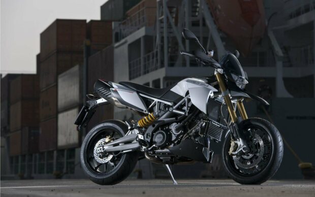 A sleek Aprilia motorcycle with detailed components and a modern frame parked near cargo containers, HD Desktop Wallpaper