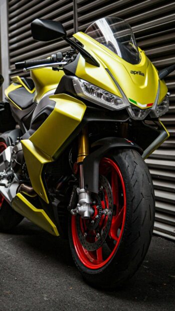 A close up view of a sleek yellow Aprilia motorcycle with red wheels parked on the street, 2K Phone Wallpaper