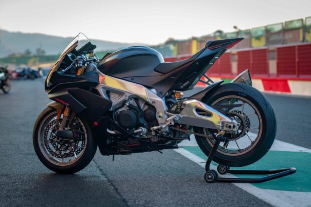 A sleek Aprilia motorcycle is parked on a race track with mountains in the background, 2K Desktop Wallpaper
