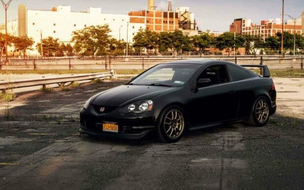A black Honda Integra is parked on an asphalt surface with industrial buildings in the background, HD Desktop Wallpaper