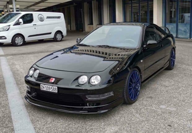 A sleek black Honda Integra with distinct blue wheels parked on a concrete surface near a building, HD Desktop Wallpaper