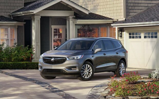 A silver Buick Enclave is parked in a driveway outside a suburban house with flowers nearby, 2K Desktop Wallpaper