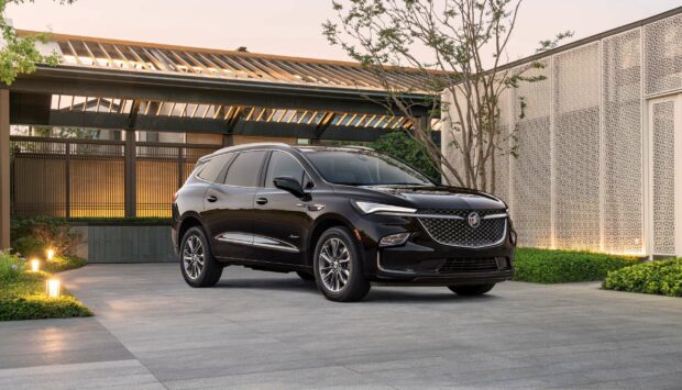 A sleek black Buick Enclave parked in a stylish driveway near a modern building at sunset, 2K Desktop Wallpaper