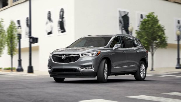 A gray Buick Enclave drives confidently through an urban intersection with blurred background trees and street lamps, 4K Desktop Wallpaper