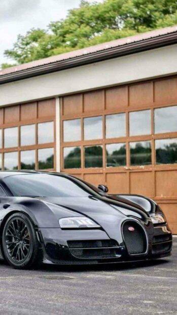 A sleek black Bugatti Veyron is parked in front of a building with large wooden garage doors, HD Phone Wallpaper