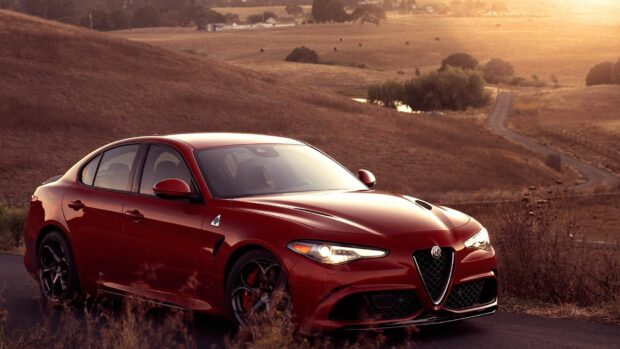 A sleek red Alfa Romeo is parked on a country road during sunset with golden fields in the background, 2K Desktop Wallpaper