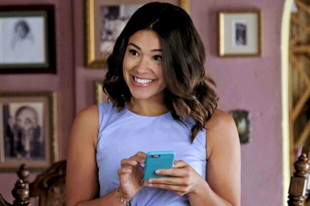 A joyful woman holds a smartphone and smiles brightly in a warm room, 2K Desktop Wallpaper