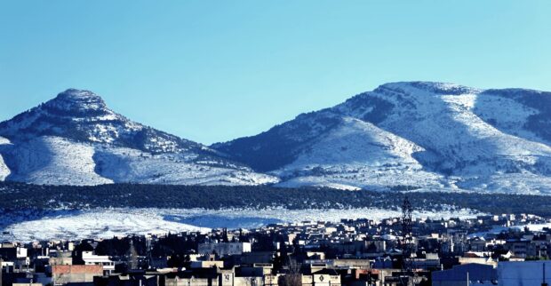 A clear view of snow covered mountains above a city in Algeria showcases natural beauty and urban life, 4K Desktop Wallpaper